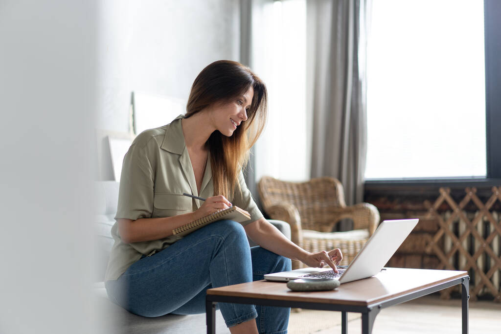 Egy nő laptopot használ a nappalijában. Otthonról dolgozom a karanténban. Társadalmi távolság. - Fotó, kép
