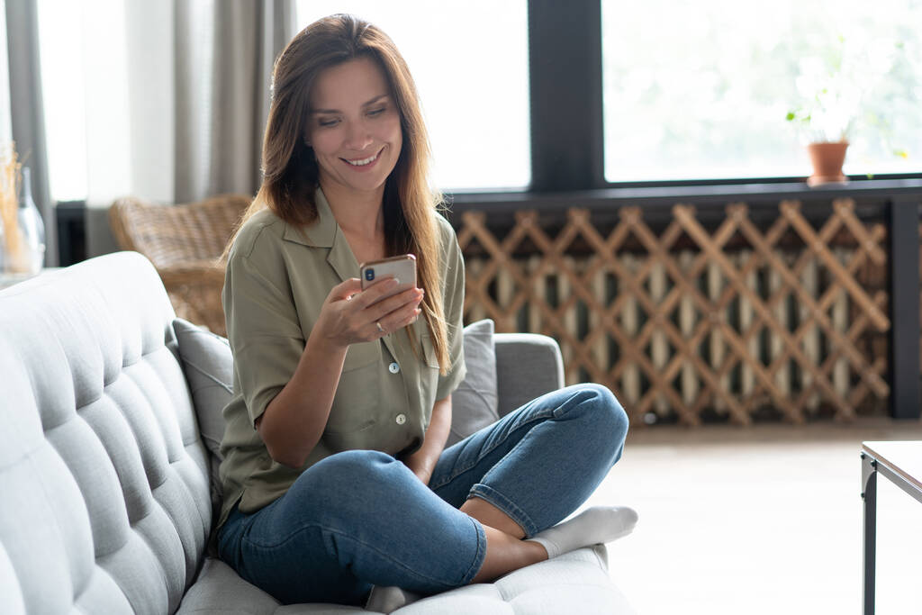Mujer usando portátil y teléfono móvil en el sofá. - Foto, Imagen