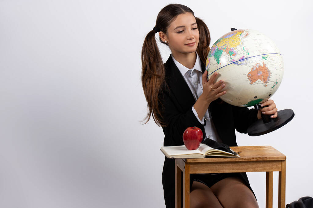 Dívka, která drží model zeměkoule, se na něj podívá. Izolované bílé pozadí s prázdným místem. Kvalitní fotografie - Fotografie, Obrázek