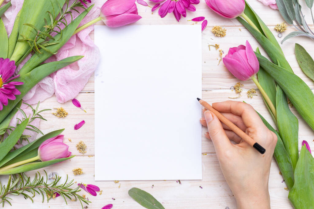 紫色の花で飾られた空白の紙に女性の手の書き込みのトップビュー - 写真・画像