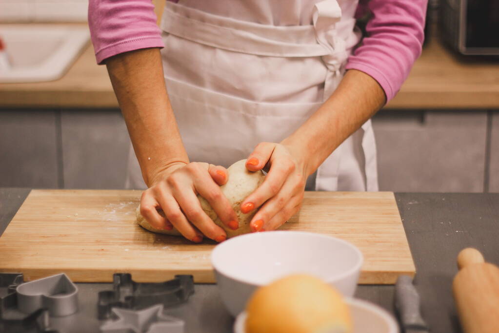 A kezek a tésztával dolgoznak, hogy friss gyömbérsütit készítsenek. A női kezek tésztát készítenek házi sütikhez egy fából készült asztalon, liszttel megszórva. A nők kezei nyújtják ki a dohányt. - Fotó, kép