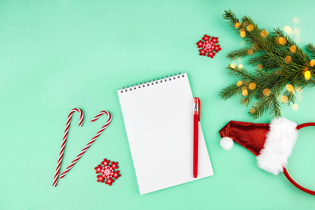 Christmas composition, wish list concept. Notebook with pen, spruce branches, decoration on green background. Flat lay, top view. - Photo, Image