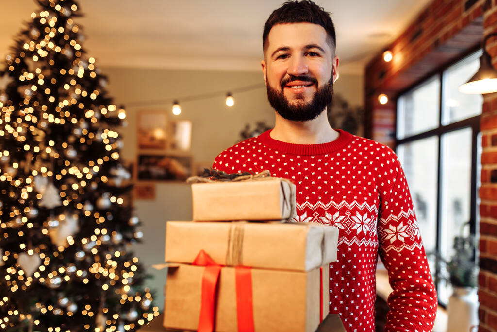 heureux jeune homme dans le pull de la nouvelle année, avec de nombreuses boîtes-cadeaux à la maison, joyeux Noël - Photo, image