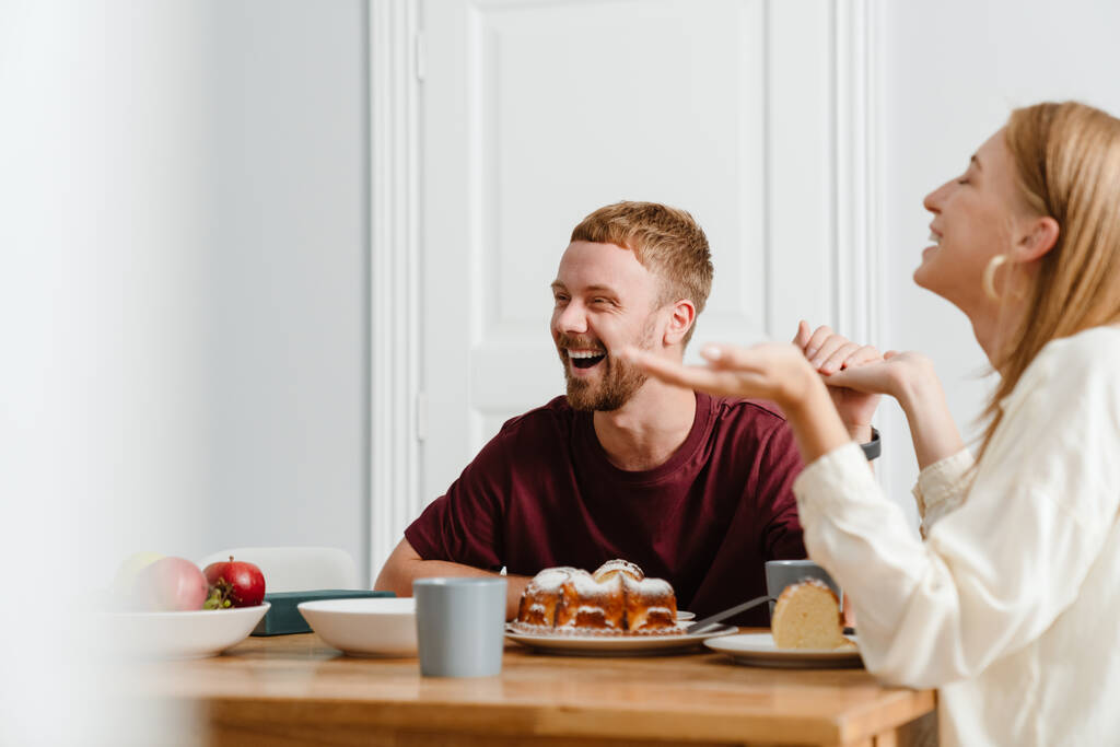 Fotografie radostný krásný pár mluvit při pití čaje s koláčem v kuchyni - Fotografie, Obrázek