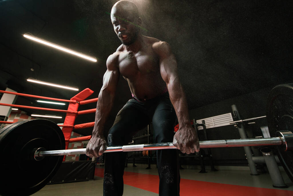 М'язистий афроамериканський чоловік важкоатлет або культурист робить вправи з барбелом в тренажерному залі
 - Фото, зображення