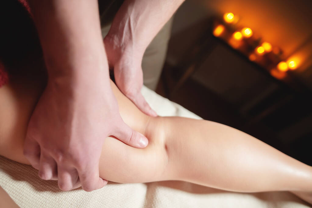 Mężczyzna masażysta robi masaż uda i dolnej nogi kobiecie klientce w ciemnym pokoju gabinetu masażu - Zdjęcie, obraz