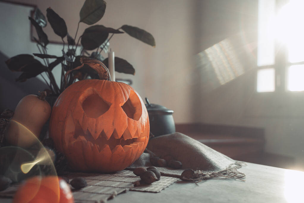 Cara de abóbora assustadora de Halloween com vela acesa em uma mesa e luz solar. Esqueleto, velas, nozes. Teal e laranja bela natureza morta. - Foto, Imagem