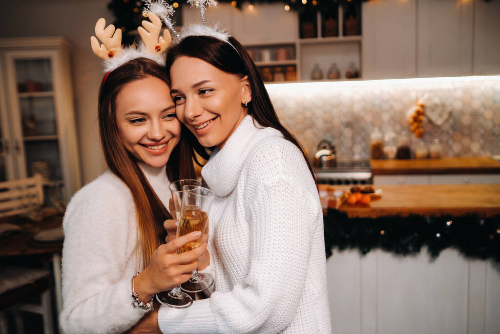 two girls in a cozy home environment with champagne in their hands at Christmas. Smiling girls drink champagne on a festive evening. - Photo, Image