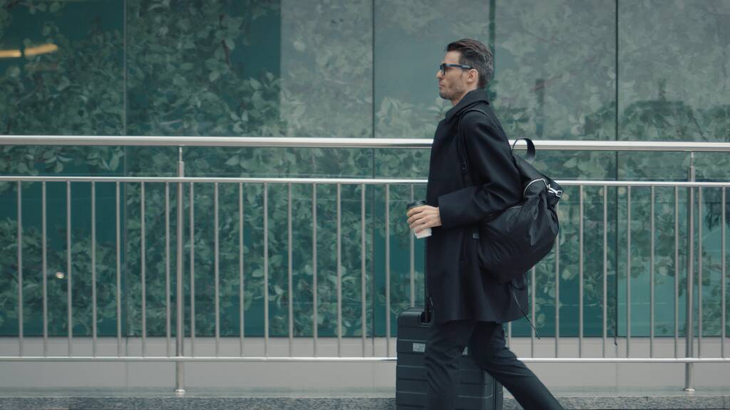 Mies musta takki matkalaukku kävely taustalla lasi-ikkunat - Valokuva, kuva