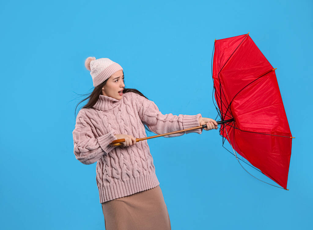Young woman with umbrella caught in gust of wind on light blue background - Photo, Image