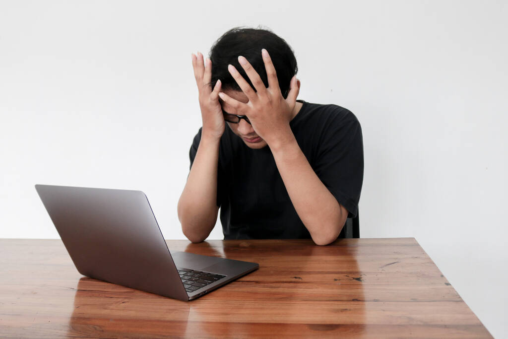 Genç Asyalı bir adam stres hissediyor ve laptoptaki işiyle karıştırıyor. Endonezyalı adam siyah gömlek giyer. Gri arka plan.. - Fotoğraf, Görsel