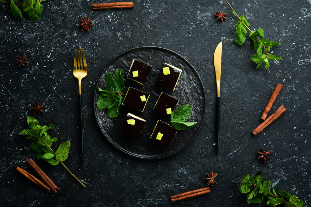 Шоколадный десерт из мусса Опера на черной тарелке с мятой. Вид сверху. Сельский стиль. - Фото, изображение