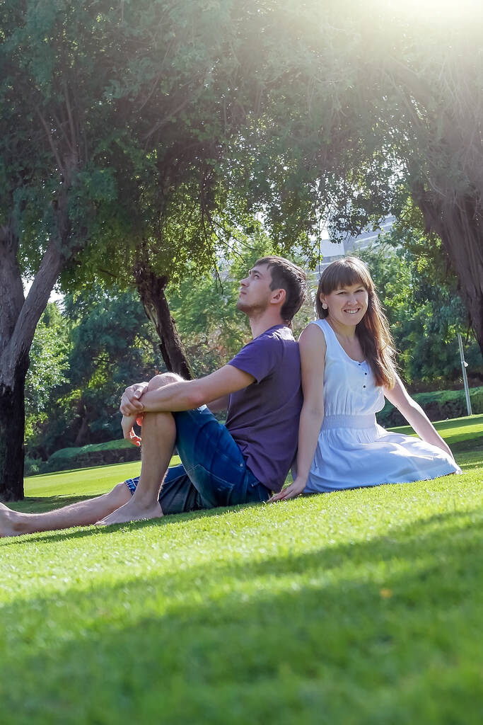 愛するカップルは、晴れた日に公園の芝生の上に、カメラを見て横たわっている。新婚旅行の幸せな若い女性と男。ロマンチックなライフスタイル - 写真・画像
