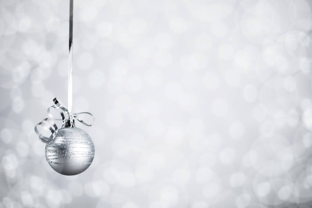 Silver Christmas new year ball with curly streamer ribbon bow over glittering bokeh lights background with copy space for text - Photo, Image