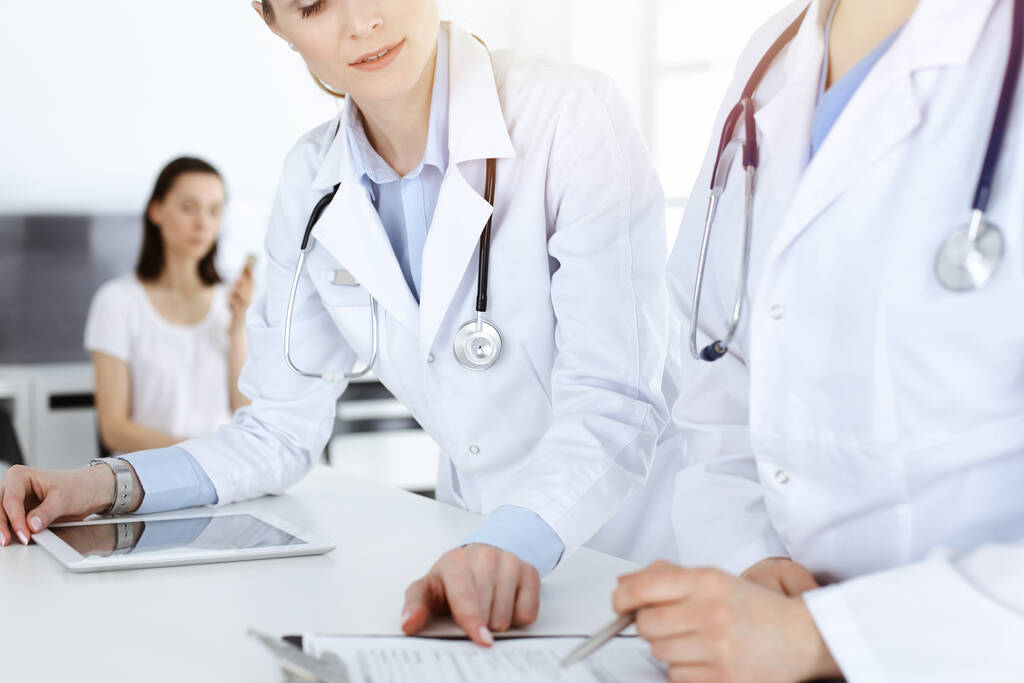 Dvě ženy-doktoři v práci s pacientem v pozadí. Lékařky plní lékařské dokumenty nebo předpis, zatímco stojí na recepci nemocnice. Údaje v medicíně - Fotografie, Obrázek