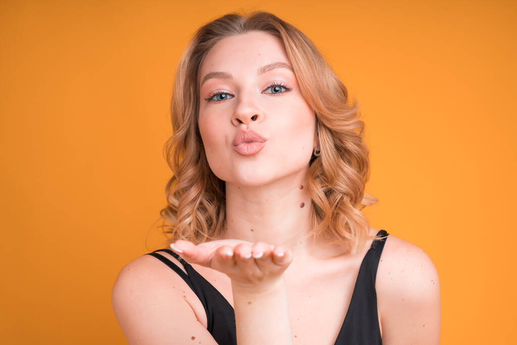 На рекламі зображена приваблива блондинка Кавказька молода жінка з натуральним макіяжем, який дув поцілунок, ізольований на помаранчевому тлі. - Фото, зображення