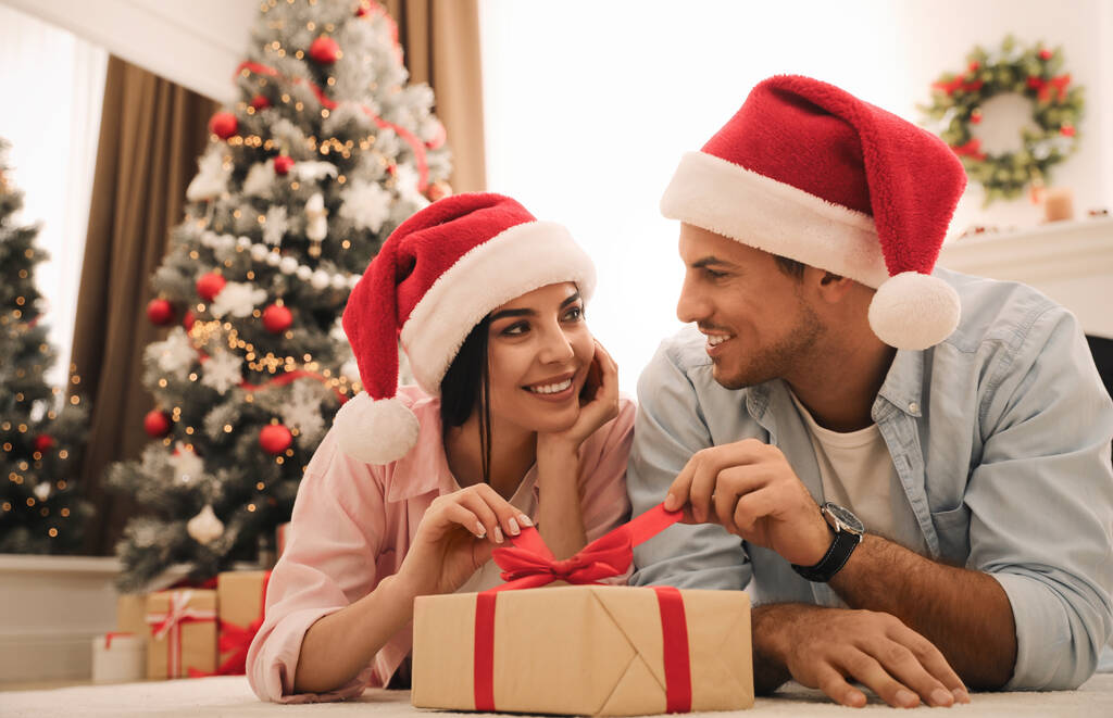 Gelukkig paar in Santa hoeden met kerstcadeau thuis - Foto, afbeelding