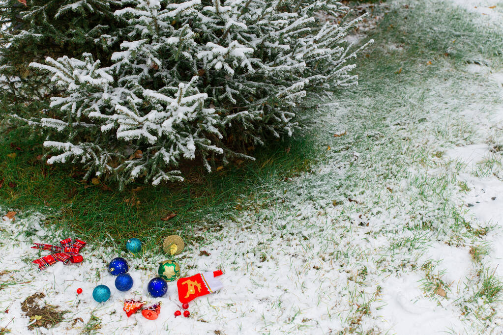 Барвисті новорічні іграшки лежать на снігу біля дерева. Концепція підготовки до святкування Різдва та Нового року та прикраси ялинки
 - Фото, зображення
