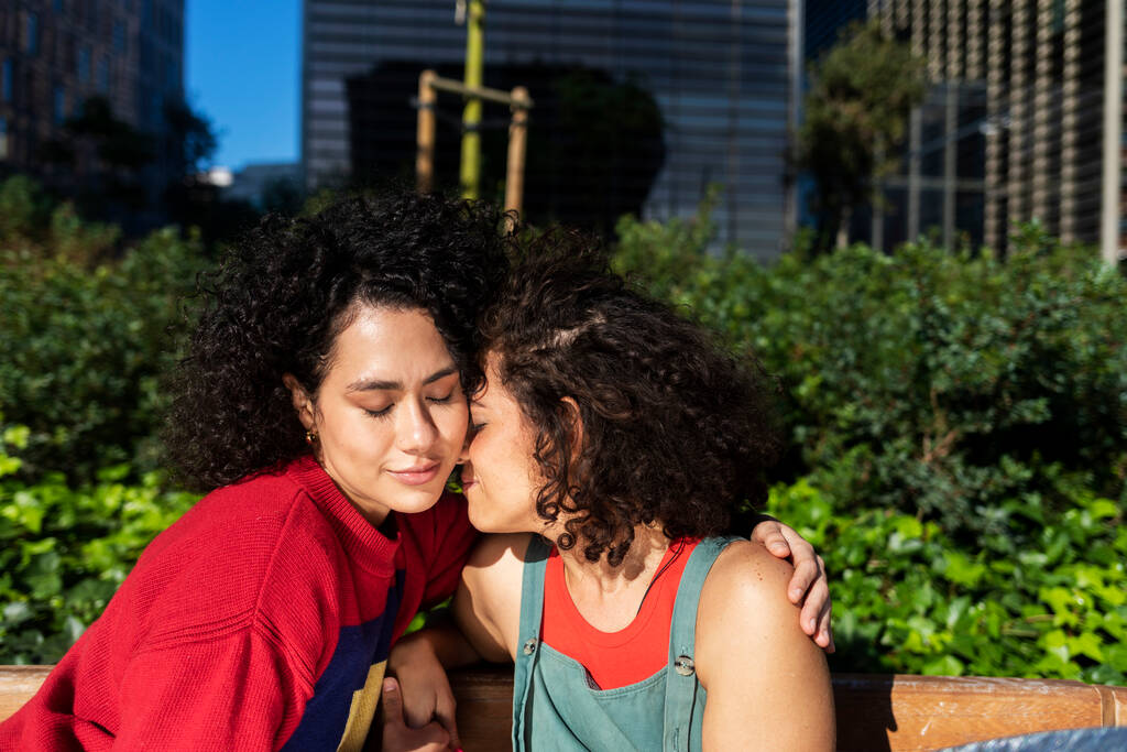 Lächelndes lesbisches Paar umarmt und entspannt sich auf einer Parkbank - Foto, Bild