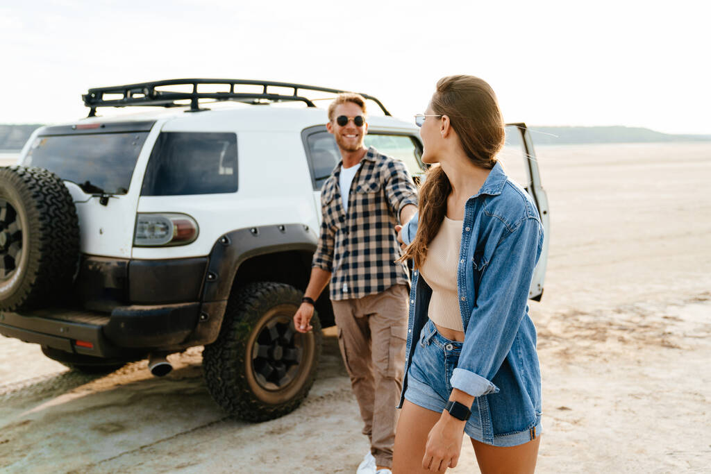 Молодая счастливая любящая пара на открытом воздухе на пляже рядом с автомобилем ходьба, объятия, держась за руки - Фото, изображение