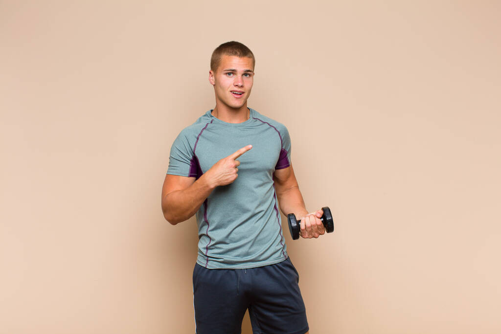 young blonde man looking excited and surprised pointing to the side and upwards to copy space - Photo, Image