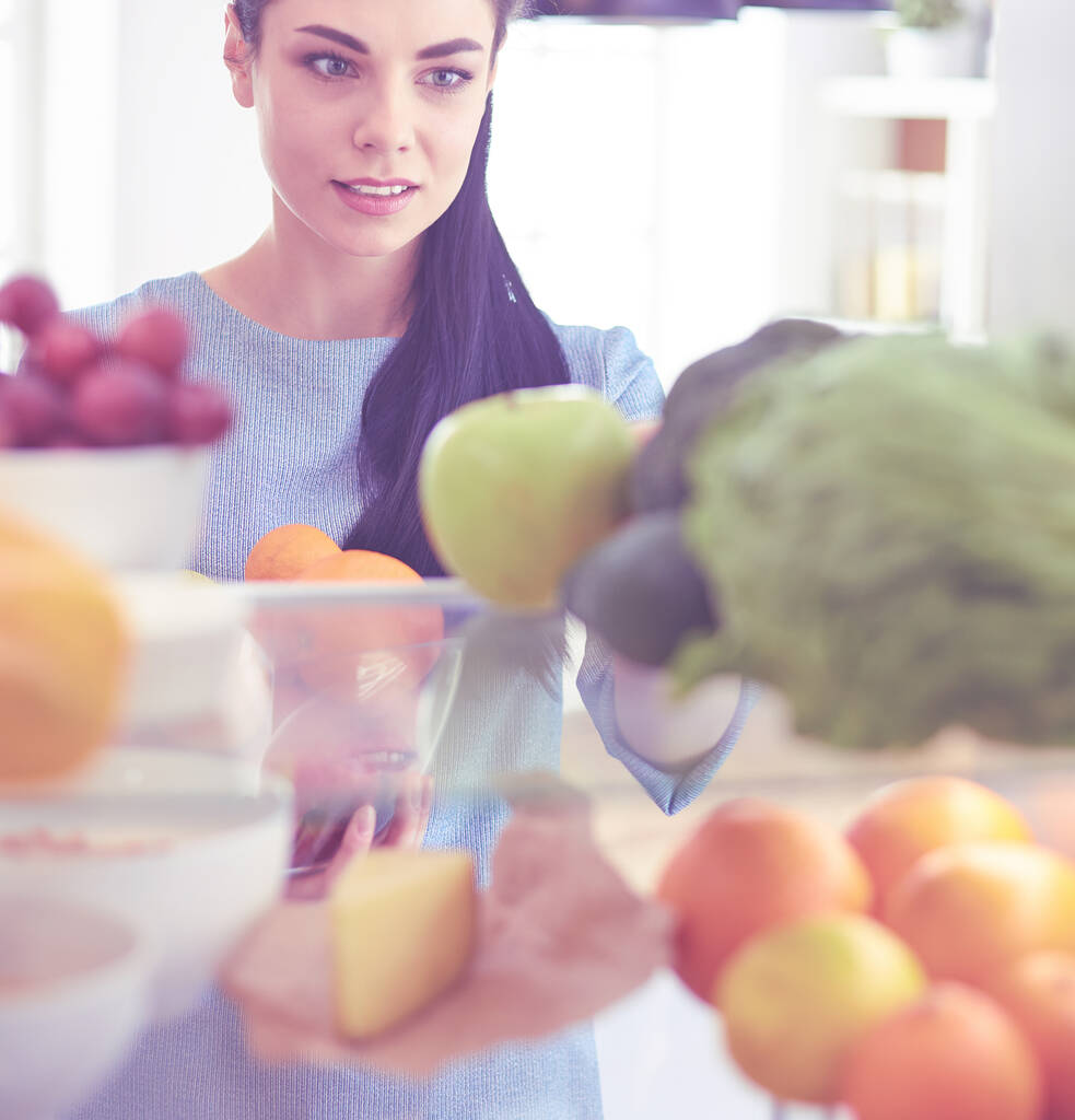 Hymyilevä nainen ottaa tuoreita hedelmiä jääkaapista, terveellistä ruokaa käsite - Valokuva, kuva