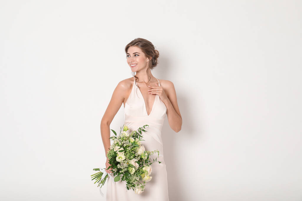 若い花嫁は、光の背景に美しい花束で結婚式のドレスを着て - 写真・画像