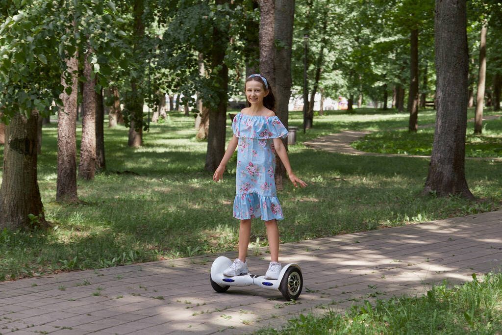 Una chica con un vestido azul pasea por el parque en un scooter giratorio. Cabello largo. - Foto, imagen