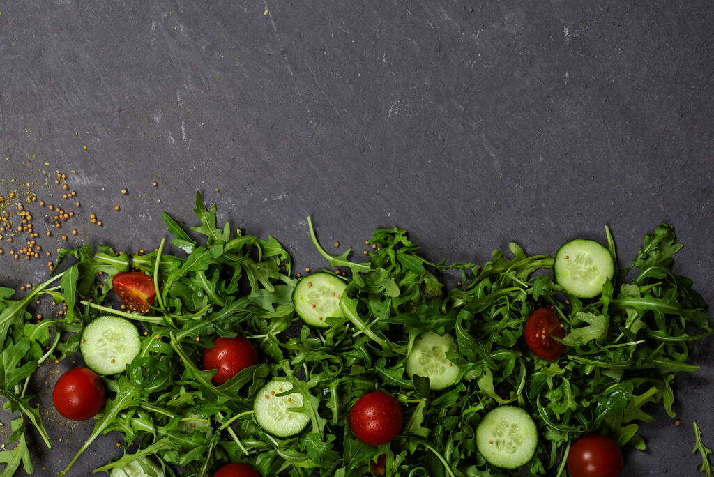 Свежие овощи руккола, помидор, огурец, травы, перец и оливки на горизонтальном темно-сером текстурированном фоне. Вид сверху. Место для текста, - Фото, изображение