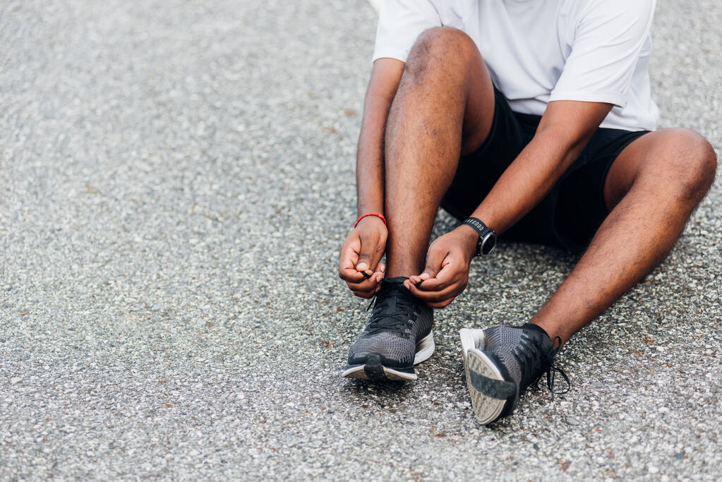 Κοντινό πλάνο ασιατικό δρομέας μαύρο άνδρα φορούν ρολόι κάθεται προσπαθεί κορδόνια τρέξιμο παπούτσια ετοιμάζεται για τρέξιμο και να τρέξει υπαίθριο πάρκο υγείας δρόμο με αντίγραφο χώρο, υγιή άσκηση έννοια προπόνηση - Φωτογραφία, εικόνα
