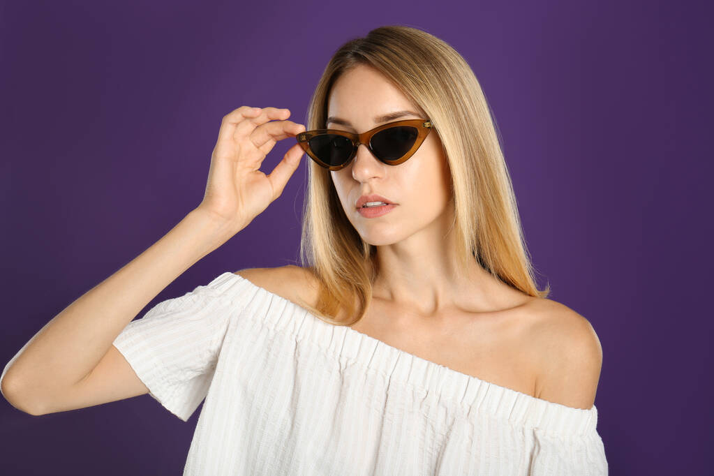 Belle femme dans des lunettes de soleil élégantes sur fond violet - Photo, image