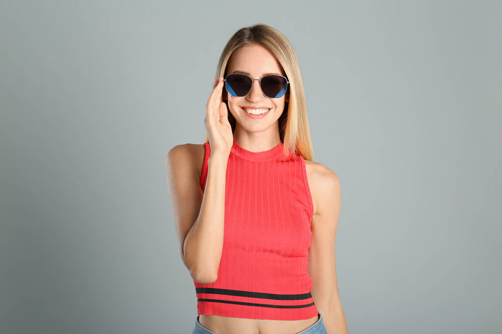Mooie vrouw in stijlvolle zonnebril op grijze achtergrond - Foto, afbeelding