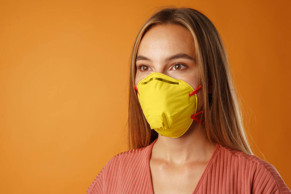 Jeune belle femme décontractée portant un masque médical protecteur de couleur jaune éclairant - Photo, image