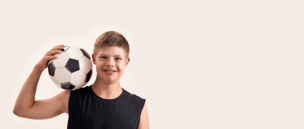 Joyful disabled boy with Down syndrome smiling at camera while posing with football isolated over white background - Photo, Image