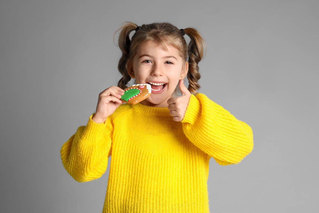 Linda niña con galleta de jengibre de Navidad sobre fondo gris claro - Foto, Imagen