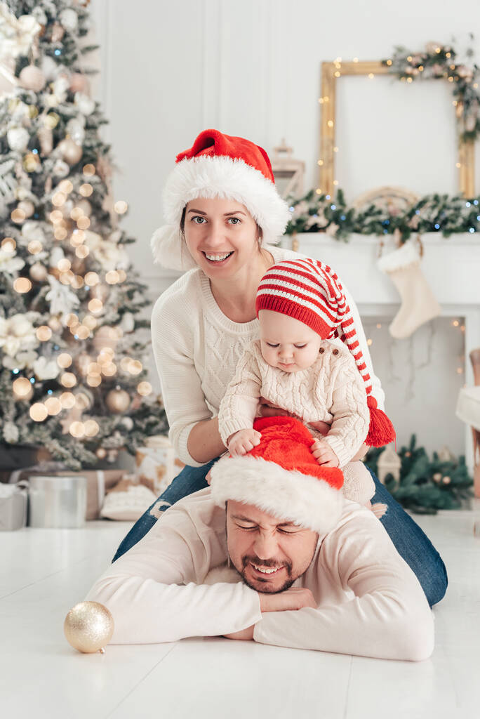 Счастливая семья под елкой. мальчик в шляпе Санта-Клауса с подарками под елкой со многими подарками коробки. Счастливых праздников, Новый год. Уютный теплый зимний вечер дома. Рождественское время - Фото, изображение