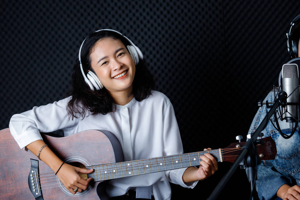 Felice allegro bel sorriso del ritratto della giovane cantante asiatica che indossa le cuffie con una chitarra che registra una canzone davanti al microfono in uno studio professionale - Foto, immagini