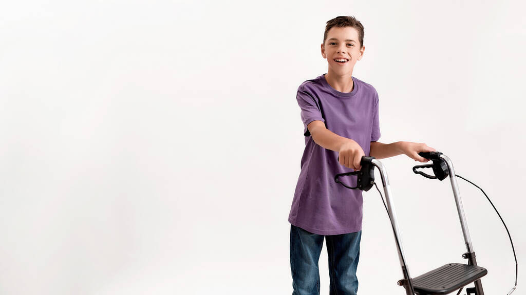 Щасливий хлопчик-підліток з інвалідністю з церебральним паралічем посміхається на камеру, робить кроки, використовуючи його ходунки ізольовані на білому тлі
 - Фото, зображення