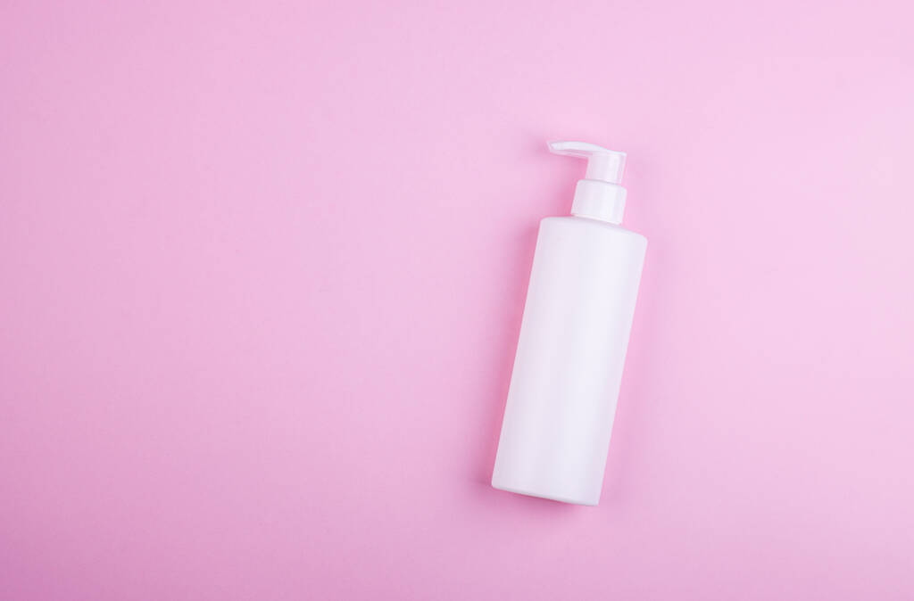 Produkt péče o tělo v bílé láhvi na růžovém pastelovém pozadí. Pohled shora, místo pro text - Fotografie, Obrázek