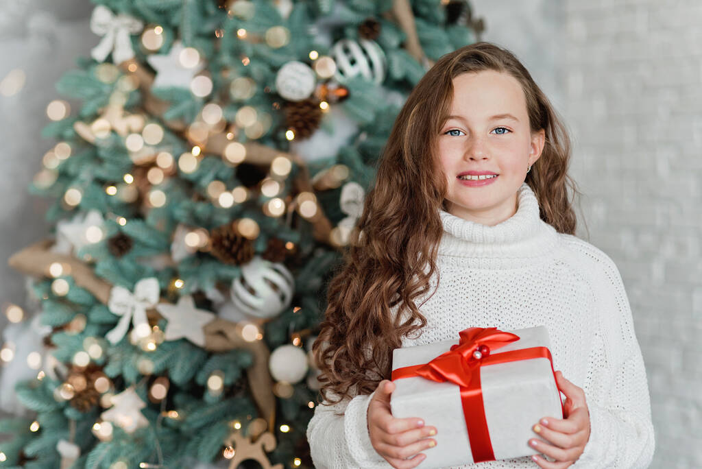 Szczęśliwe podekscytowane dziecko trzyma pudełko prezentów świątecznych. Dziecko z prezentem świątecznym w urządzonym pokoju. Koncepcja Bożego Narodzenia i ludzi. Szczęśliwego Nowego Roku. dziecko zadowolone z teraźniejszości. - Zdjęcie, obraz
