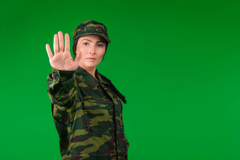 Yeşil arka planda, askerî üniformalı ciddi bir kadın ve boş alan şovları duruyor. Sağlık ve salgın hastalık. Yüksek kalite fotoğraf - Fotoğraf, Görsel