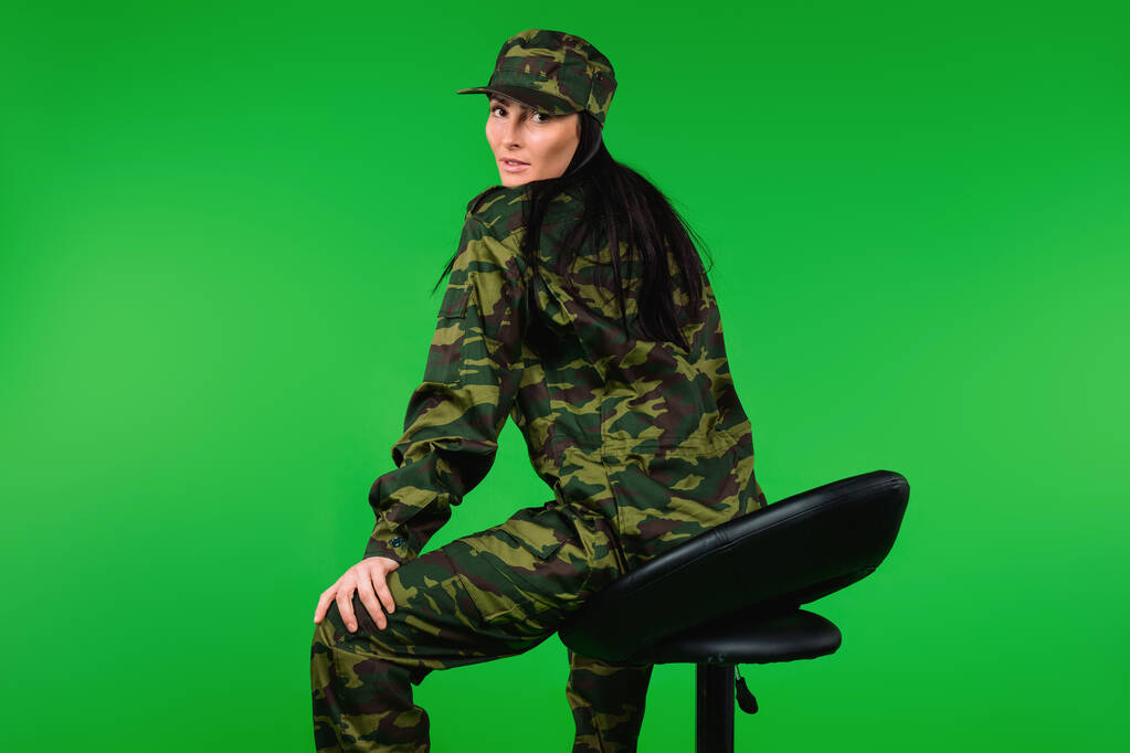 Фото ззаду. Жінка в військовій формі позує на чорному стільці. Зелений фон. Високоякісна фотографія
 - Фото, зображення