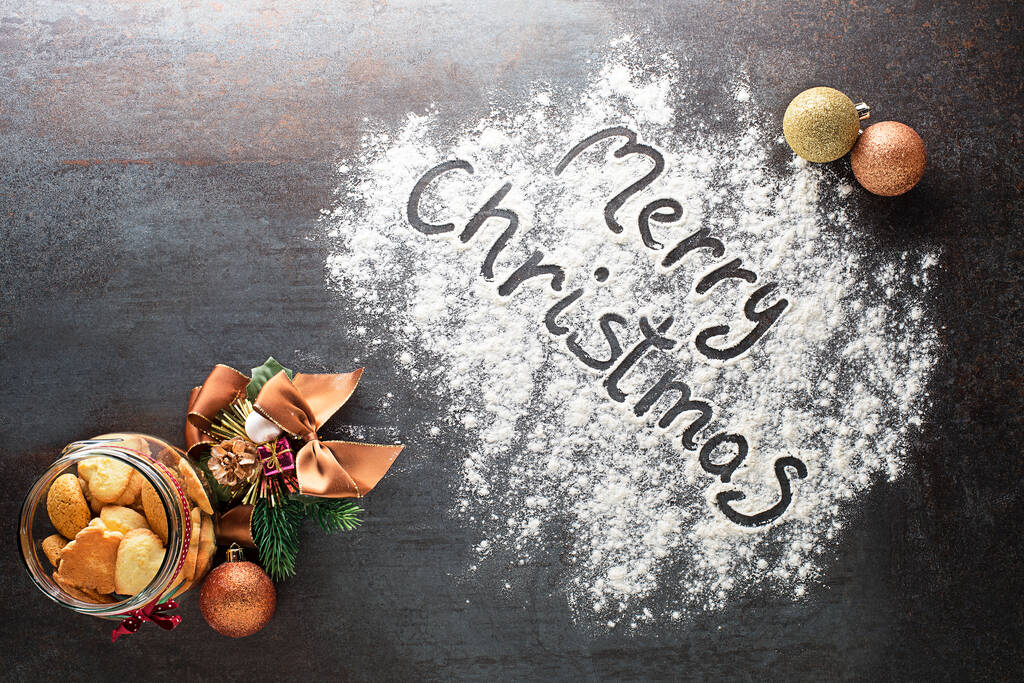装飾品やクッキーと小麦粉で作られたメリークリスマスのテキスト。クリスマス、冬、新年のコンセプトの背景. - 写真・画像