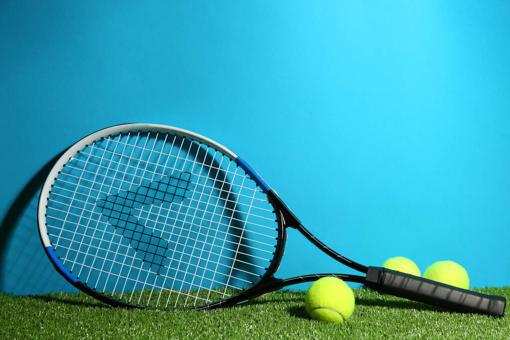 ρακέτα τένις και μπάλες σε πράσινο γρασίδι σε γαλάζιο φόντο. Χώρος για κείμενο - Φωτογραφία, εικόνα