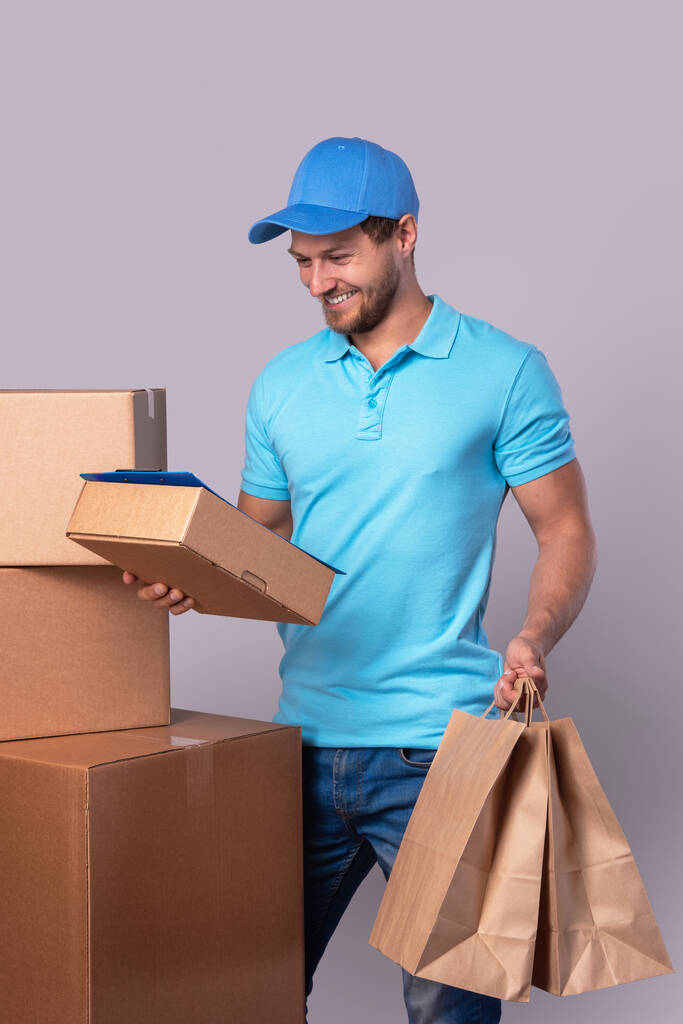 Happy delivery man κατά τη διάρκεια της εργασίας με πακέτα σε χαρτονένια κουτιά πάνω από γκρι φόντο - Φωτογραφία, εικόνα