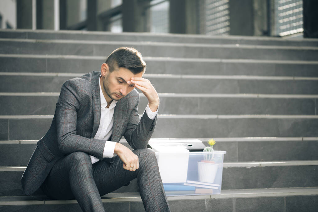 Verzweifelte männliche Büroangestellte verloren ihren Job. Trauriger Geschäftsmann, der mit einer Schachtel voller Sachen auf einer Treppe im Freien sitzt. Feuriger Mann. Arbeitslosenquote steigt wegen Pandemie - Foto, Bild