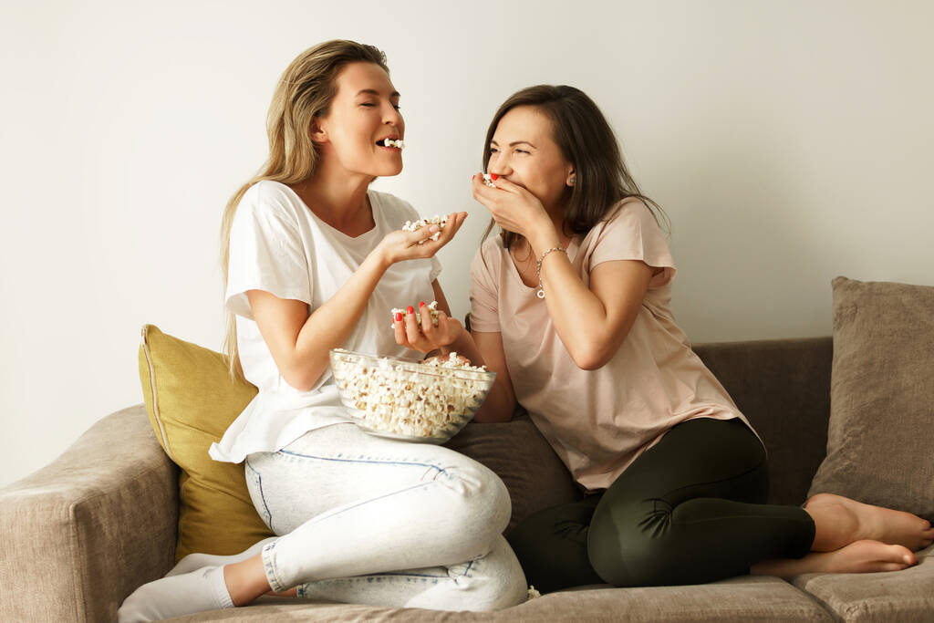 Zwei schöne Freundinnen gucken Fernsehshow und essen Popcorn zu Hause - Foto, Bild