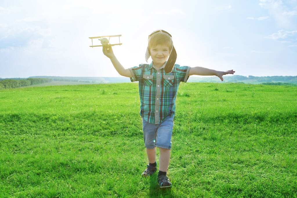 Ξεκινήστε να ταξιδεύετε από την παιδική ηλικία ακόμα και στη φαντασία. χαρούμενο παιδί ονειρεύεται να ταξιδέψει και να παίξει με έναν πιλότο αεροπλάνου σε εξωτερικό χώρο το καλοκαίρι. - Φωτογραφία, εικόνα