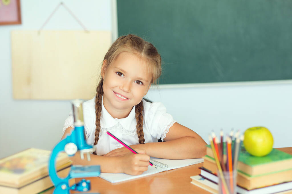 Kleines Mädchen zeichnet oder schreibt mit Buntstiften in Notizbuch in der Schule über Tafel. - Foto, Bild