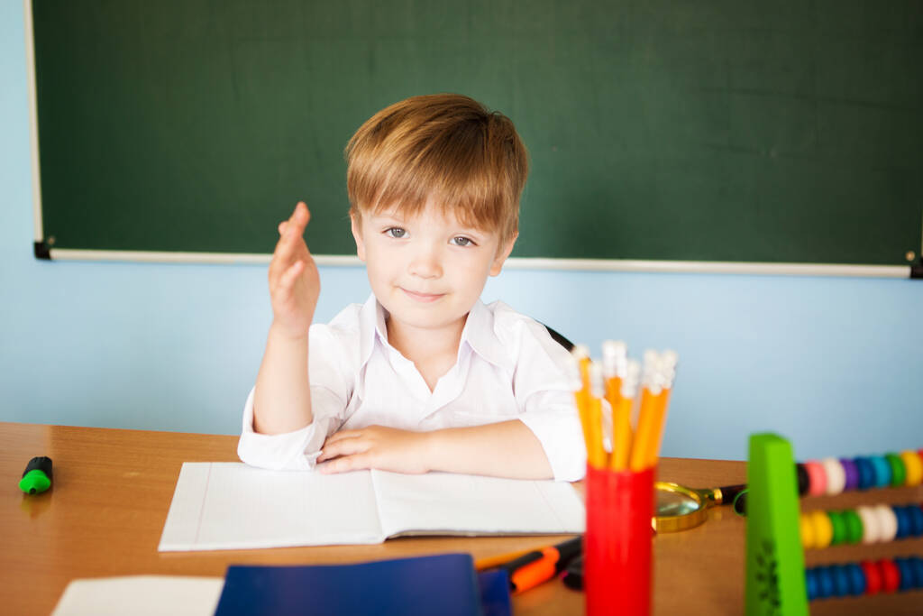 Маленький милий хлопчик в школі готовий відповісти на урок і підтягує руку вгору
 - Фото, зображення